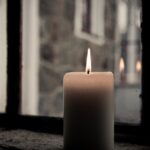 A lit candle by a window, offering a warm and cozy ambiance.